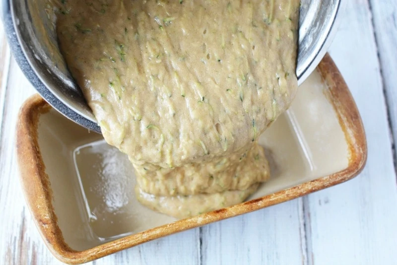 Pouring zucchini mixture into loaf pan for zucchini bread