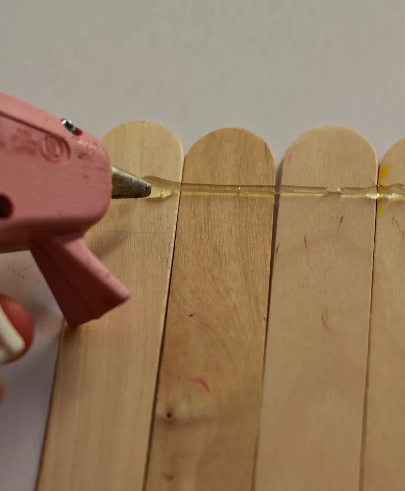 Hot glue gun with popsicle sticks to make DIY Pencil Frame