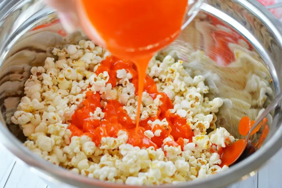 Pouring mixture onto popcorn for candied popcorn