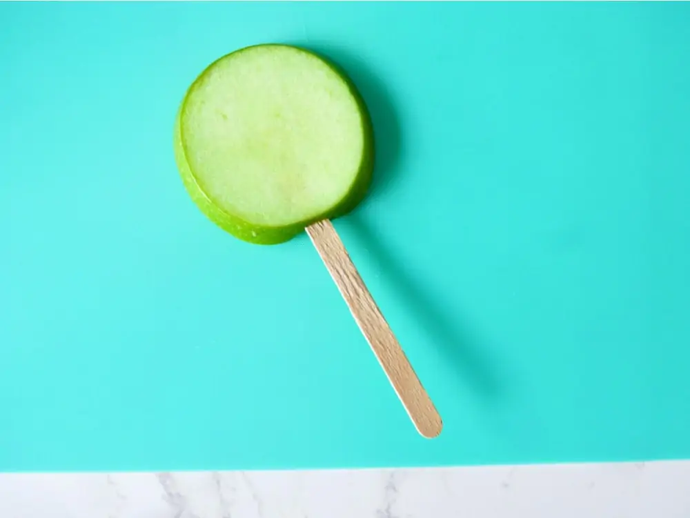 Sticking popsicle stick in apple for caramel apple pops