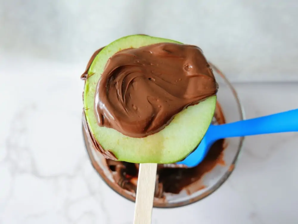 Adding chocolate to apples for caramel apple pops