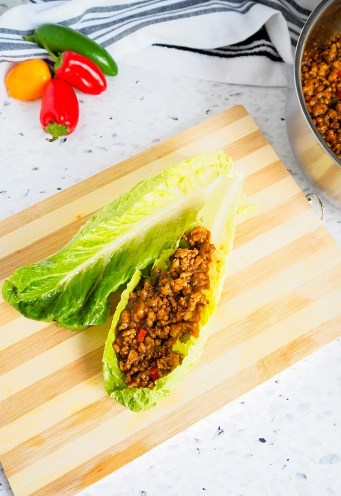 Adding cooked chicken to lettuce for lettuce wraps