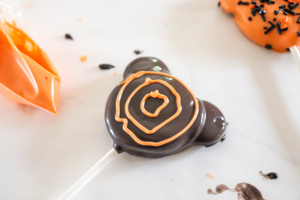 Adding circles with orange icing to halloween oreo pops